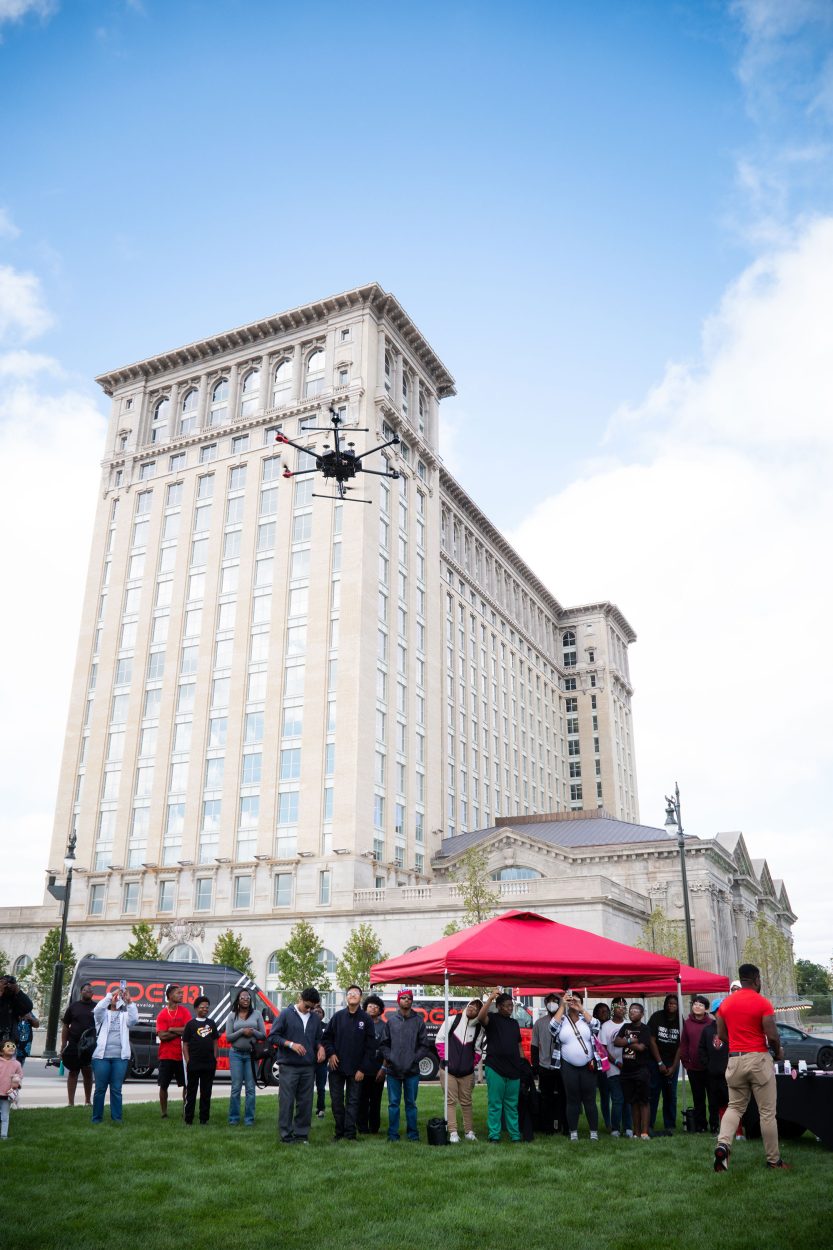 A drone operated by attendees at the Drone Day event hovers near The Station.