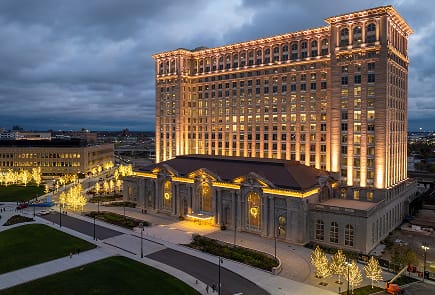 Michigan Central Station illuminated at night with golden lights highlighting its architectural details.