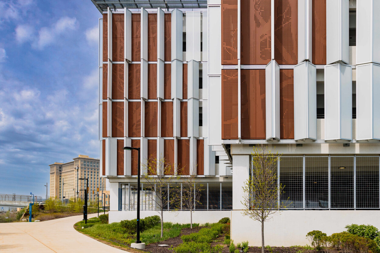 Close-up of the upper floors of a contemporary building facade featuring vertical wooden slats and large glass windows with a grid pattern, set against a blue sky.